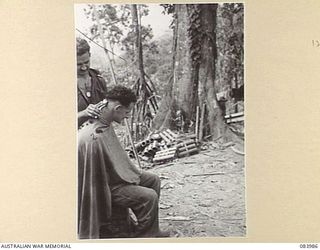 BOUGAINVILLE, SOLOMON ISLANDS. 1944-12-13. PRIVATE S. GRIFFITHS, (2), RECEIVES A HAIRCUT FROM PRIVATE G.L. SILVER, (3), 9 INFANTRY BATTALION. MORTAR CASES ARE SEEN AT THE BACKGROUND