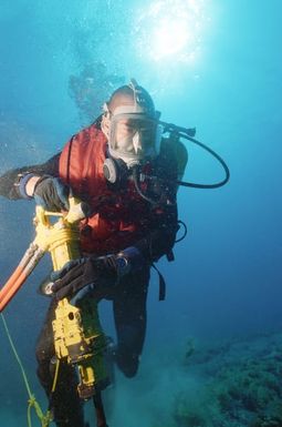 MASTER CHIEF (UCCM) Michael R. Oliver of Underwater Construction Team Two (UCT-2) drills holes in the coral bed next to the cable so that clamps can be placed for stabilization at the Pacific Missile Range Facility at Kauai, Hawaii