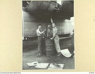 LAE-NADZAB, NEW GUINEA. 1944-07-20. PRIVATE W. ROOKE (1) AND PRIVATE A. CLARKE (2) 2ND AUSTRALIAN CORPS SALVAGE UNIT DRAWING THE OIL FROM THE TANKS OF A UNITED STATES ARMY AIR CORPS CONSOLIDATED ..