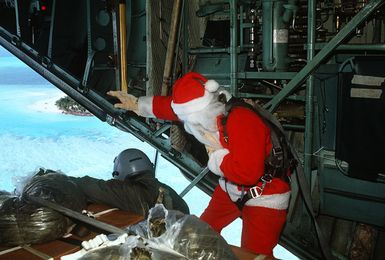 Santa Clause (CAPT. Mike d'Albertis, 605th Military Airlift Support Squadron) and STAFF SGT. Tony Thompson, loadmaster with the 21st Tactical Airlift Squadron, watch as a Christmas Drop container is parachuted toward its destination. The annual airdrop is a humanitarian effort providing aid to needy islanders throughout Micronesia during the holiday season