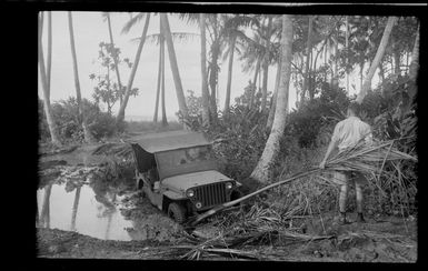 An unidentified RNZAF airman with a jeep that has become stuck in the mud, Guadalcanal, Solomon Islands