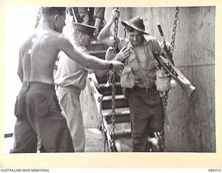 CUTARP PLANTATION, JACQUINOT BAY, NEW BRITAIN. 1944-12-15. A HEAVILY LADEN SOLDIER FROM A COMPANY, 19 INFANTRY BATTALION BEING ASSISTED FROM THE GANGWAY OF THE TROOPSHIP FRANCIS PARKMAN