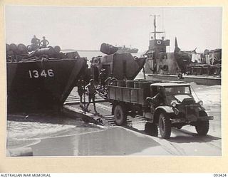 AITAPE BEACH HEAD, NEW GUINEA. 1945-06-19. MEMBERS OF 7 DOCKS OPERATING COMPANY, ROYAL AUSTRALIAN ENGINEERS, WATCH AS A TRUCK BACKS UP THE RAMP OF A LANDING CRAFT, TANK (LCT) LOADED WITH FUEL FOR ..