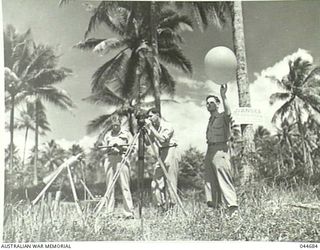PILOT BALLOON ASCENT MILNE BAY, NEW GUINEA, 1945. FLYING OFFICER W. JORDON (QUEENSLAND) CALCULATING WIND FORCE AND DIRECTION ON SLIDE RULE, METEOROLOGICAL ASSISTANTS LAUNCHING BALLOON AND OPERATING ..