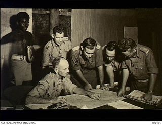 Bisiatabu, New Guinea. 1944-05-22. Major E. A. F. Stanfield, Commanding Officer, 1 Papuan Infantry Battalion, holding a conference at his unit HQ. Left to right: Corporal Boski; Lieutenant (Lt) R. ..