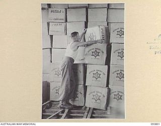 LAE AREA, NEW GUINEA, 1945-07-11. PRIVATE H.J. CROWLEY AT THE AUSTRALIAN COMFORTS FUND, LAE DISTRIBUTION CENTRE, CHECKING HAMPERS BEFORE THEIR MID-YEAR DISTRIBUTION IN THE LAE AREA AND THEIR ..