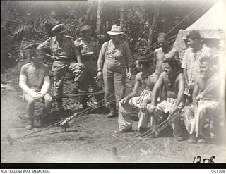 HOLLANDIA, DUTCH NEW GUINEA. C. 1944-06. THE MINISTER FOR AIR, ARTHUR DRAKEFORD (CENTRE, IN HAT), FLIGHT LIEUTENANT F. PRESCOTT, SQUADRON LEADER (SQN LDR) E. RYAN, MELBOURNE, VIC, SQN LDR R. ALDER, ..