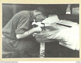 MILILAT, NEW GUINEA. 1944-08-01. VX136048 SAPPER D.P. FARR USING A TYPE B3 STEREOSCOPE ON RAAF AERIAL PHOTOGRAPHS IN THE PHOTO INTERPRETATION ROOM, INTELLIGENCE SECTION, HEADQUARTERS, 5TH DIVISION