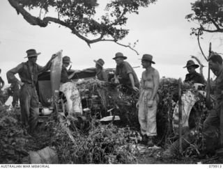 DAGUA, NEW GUINEA. 1945-03-25. MEMBERS OF B COMPANY 2/2 INFANTRY BATTALION ALONGSIDE THEIR "DOOVERS" (SHELTERS) BESIDE ABANDONED JAPANESE AIRCRAFT ENGINES ON THE AIRSTRIP. IDENTIFIED PERSONNEL ..