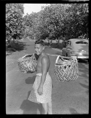Unidentified boy carrying items in woven baskets, Samoa