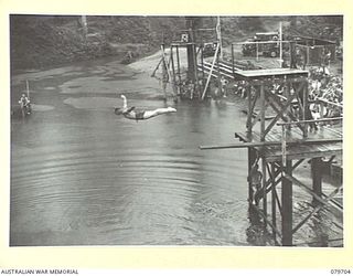 TOROKINA, BOUGAINVILLE, SOLOMON ISLANDS. 1945-03-10. PRIVATE RASMUSSEN, 57/60TH INFANTRY BATTALION WATCHED BY COMPETITORS IN THE BACKGROUND, EXECUTES A DIVE DURING THE SWIMMING CARNIVAL CONDUCTED ..