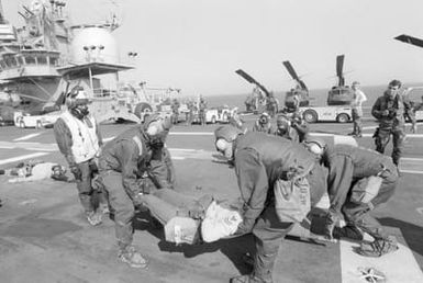 Crew members wearing nuclear, biological and chemical warfare gear transport a"casualty"from the flight deck of the amphibious assault ship USS GUAM (LPH 9) during field training Exercise SOLID SHIELD'87