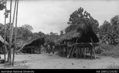 Two buildings on stilts, two European men in background