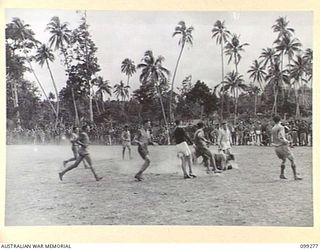 RABAUL, NEW BRITAIN, 1945-12-01. A RUGBY FOOTBALL GAME IN PROGRESS BETWEEN MEMBERS OF 2/2 COMMANDO SQUADRON AND HQ 11 DIVISION AT 4 INFANTRY BRIGADE OVAL. SPORT IS PLAYED EACH AFTERNOON BY THE ..