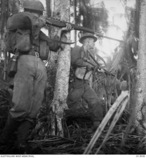 1942-12-28. PAPUA. INFANTRY BACK UP ATTACK ON BUNA BY AUSTRALIAN MANNED GENERAL STUART TANKS. THE AUSTRALIAN IN THE PHOTO IS FIRING AN M1 GARAND RIFLE AT JAPS IN A PILLBOX 30 YARDS AWAY. HE GOT ..
