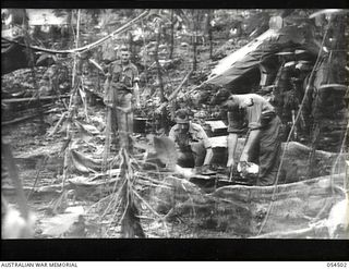 Mubo-Salamaua Area, New Guinea. 1943-07-22. Troops using primitive cooking facilities at the Headquarters Camp of the 2/5th Australian Infantry Battalion, AIF. Left to right: VX29920 Private A.J. ..