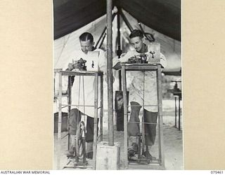 MILILAT, NEW GUINEA. 1944-08-23. QX15601 CORPORAL R.E. NORRIS (1) AND NX99092 STAFF SERGEANT O.G. MCDONALD (2), DENTAL MECHANICS, 77TH DENTAL UNIT, GRINDING ARTIFICIAL DENTURES IN THE UNIT WORKSHOP