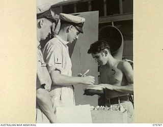 HUMBOLT BAY, NEW GUINEA. 1944-09/08. RATINGS BEING "PAID OVER THE CAP" IN THE OLD NAVAL TRADITIONAL MANNER ABOARD THE RAN CORVETTE, GEELONG