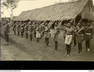 Bisiatabu, New Guinea. 1944-5-22. Sergeant W. Wall, 1 Papuan Infantry Battalion, with his platoon outside the Unit's orderly room, a thatched building