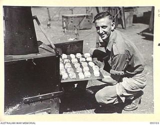 WEWAK AREA, NEW GUINEA, 1945-06-13. PTE D.J. WALPOLE, 2/2 FIELD REGIMENT REMOVING FROM A FIELD OVEN A TRAY OF SCONES HE HAS BAKED DURING A COURSE CONDUCTED BY LHQ COOKING AND CATERING SCHOOLS, AT ..