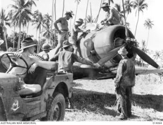Dobodura, New Guinea. 1 January 1943. Corporal John Griffiths (seated in the jeep), Corporal Herbert (Herb) Burrow (standing on the wing, working under the raised inspection cover) and an ..