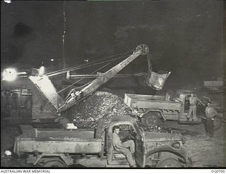 NADZAB, NEW GUINEA. C. 1944-02. MEMBERS OF NO. 62 MOBILE WORKS SQUADRON RAAF USING A STEAM SHOVEL TO LOAD GRAVEL INTO TRUCKS AT NIGHT UNDER THE BLAZE OF FLOOD LIGHTS