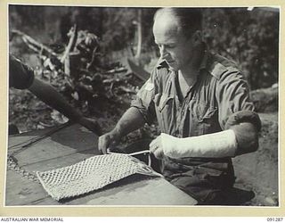 BOUGAINVILLE. 1945-04-26. CORPORAL G.D. BACKWAY, 58/59 INFANTRY BATTALION, A PATIENT AT 2/3 CONVALESCENT DEPOT, DOING STRING WORK TO EXERCISE HIS FINGERS AND WRIST WHILE HIS ARM IS STILL IN PLASTER