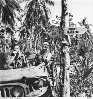 FINSCHHAFEN, NEW GUINEA. 1943. SX9267 LIEUTENANT V.E. ACOTT, DEPARTMENT OF PUBLIC RELATIONS, AND HIS DRIVER STUDY A JUNGLE SIGNPOST