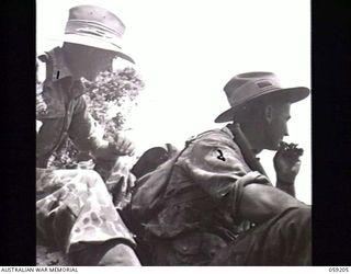LALOKI VALLEY, NEW GUINEA. 1943-11-05. MEMBERS OF A PATROL OF THE NEW GUINEA FORCE TRAINING SCHOOL (JUNGLE WING), IN THE TRIAL CAMOUFLAGED JUNGLE SUITS, REST ON A FALLEN TREE NEAR THE ROUNA FALLS. ..