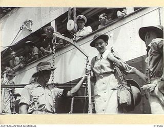 AUSTRALIAN NURSES RETURN TO NEW GUINEA. MILITARY POLICE LEND A HELPING HAND AS A SISTER EQUIPPED WITH TIN HAT, COMES ASHORE. THE SISTER HAS BEEN IDENTIFIED AS SISTER P GAME