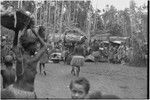 Mortuary ceremony, Omarakana: mourning women carry large baskets of banana leaf bundles for ritual exchange, especially large basket on head of woman in center background