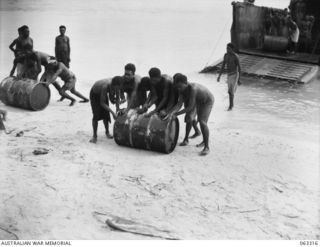 SIALUM BEACH, NEW GUINEA. 1944-01-07. NATIVES UNLOADING 44 GALLON DRUMS FULL OF PETROL AND OIL FROM THE LCM (LANDING CRAFT MECHANISED) AT THE BEACH