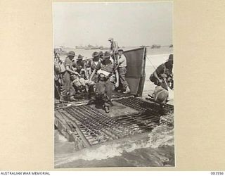 AITAPE BEACH HEAD, NEW GUINEA. 1944-11-26. GEAR LADEN 6 DIVISION STEPPING ASHORE FROM A LANDING BARGE
