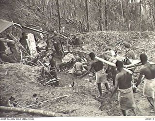 BOUGAINVILLE ISLAND. 1944-12-30. NX193746 PRIVATE J. A. HICKS, 25TH INFANTRY BATTALION, ONE OF THE EARLY CASUALTIES, ARRIVING AT THE ARTILLERY HILL REGIMENTAL AID POST ON A STRETCHER CARRIED BY ..