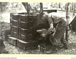 SCARLET BEACH, NEW GUINEA, 1944-03-19. Q138149 PRIVATE N. ELLIOTT (1), REMOVING BAKED JAM SLICE FROM AN OVEN CONSTRUCTED FROM A 44 GALLON DRUM AND AMMUNITION BOXES ACCUMULATED AFTER THE FIRING OF ..