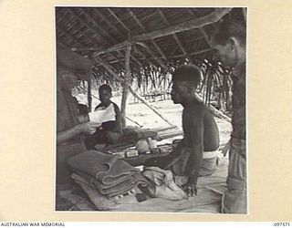 MAPRIK, NEW GUINEA. 1945-10-03. CAPTAIN M. VERSO, MEDICAL OFFICER, AUSTRALIAN NEW GUINEA ADMINISTRATIVE UNIT HEADQUARTERS, SPEAKING WITH A NATIVE WHO IS CONFINED TO BED