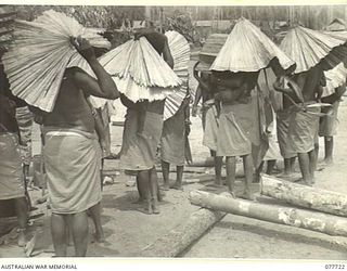 TORINKA, BOUGAINVILLE ISLAND. 1944-12-24. NATIVE WOMEN PROTECTING THEIR BABIES WITH MAKESHIFT SUNSHADES WHILE WAITING FOR THE COMMENCEMENT OF THE MASS CHRISTENING CEREMONY CONDUCTED BY ROMAN ..