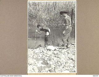 DUMPU, NEW GUINEA. 1943-11-05. VX37164 STAFF SERGEANT R. L. PRYCE OF EAST HILLS, NSW AND OF THE 2/6 AUSTRALIAN FIELD AMBULANCE, WATCHING A NATIVE TRYING TO SPEAR A FISH IN A CREEK