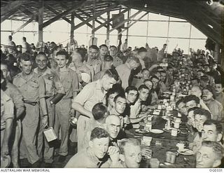 PORT MORESBY, PAPUA. 1942-12-25. RAAF CUSTOM SAYS OFFICERS SHALL BE THE AIRMEN'S WAITERS FOR CHRISTMAS DINNER. HERE IS A LINE OF OFFICERS WAITING AT THE KITCHEN FOR FOOD FOR THEIR MEN OF A JUNGLE ..