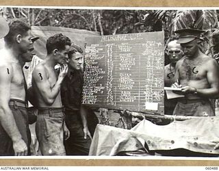 DUMPU, NEW GUINEA. 1943-11-13. TROOPS OF HEADQUARTERS, 7TH AUSTRALIAN DIVISION STUDY THE BETTING BOARD FOR THE MELBOURNE CUP. THEY ARE: UNKNOWN (1); NX168542 PRIVATE J. E. B. MADDRELL (2); VX15393 ..