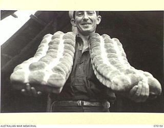 DUMPU, NEW GUINEA. 1944-02-05. VX104533 PRIVATE B.J. WALLACE (1) OF THE 24TH INFANTRY BATTALION, HANDLING FRESHLY-BAKED ROLLS AT THE 15TH INFANTRY BRIGADE BAKERY