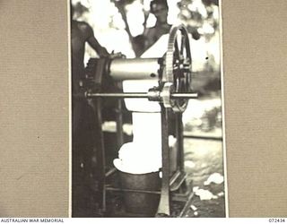 KOKODA, NEW GUINEA. 1944-04-11. NATIVES AT A RUBBER PLANTATION FEEDING RUBBER THROUGH SQUEEGEE ROLLERS TO REMOVE EXCESS WATER