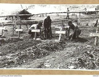 KUMBARUM, NEW GUINEA, 1943-10-23. SOLDIERS AND NATIVES PLANTING SHRUBS AROUND THE GRAVES IN THE HEADQUARTERS, 7TH AUSTRALIAN DIVISION AREA, RAMU VALLEY