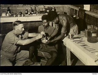Bisiatabu, New Guinea. 1944-05-22. Captain A. G. Schroeder, Regimental Medical Officer, 1 Papuan Infantry Battalion, in his surgery dressing a tropical ulcer on the leg of a native man. Left to ..