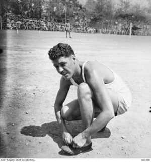 ELA BEACH, NEW GUINEA. 1943-11-13. D. LEGGETT, AN AUSTRALIAN WAR CORRESPONDENT, TYING HIS SHOE LACE BEFORE WINNING THE HIGH JUMP AT THE COMBINED SERVICES SPORTS MEETING
