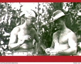 THE SOLOMON ISLANDS, 1945-02-26. AN AUSTRALIAN AND A NEW ZEALANDER COMPARE CIGARETTES AT THEIR CAMP AREA ON BOUGAINVILLE ISLAND. (RNZAF OFFICIAL PHOTOGRAPH.)