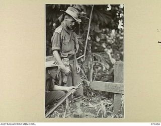ALEXISHAFEN, NEW GUINEA, 1944-05-18. TX379 LIEUTENANT E.W.J. BRANAGAN (STANDING), AND NX120747 SERGEANT R.S. MAYER, MEMBERS OF THE 35TH INFANTRY BATTALION, STAND ALONGSIDE THE GRAVE OF A NATIVE ..