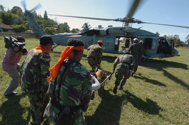 An Indonesian woman is carried to a US Navy (USN) MH-60S Seahawk helicopter, Helicopter Combat Support Squadron 5 (HC-5), Andersen Air Force Base (AFB), Guam, for medical evacuation from Nias Airport to the Military Sealift Command (MSC) Hospital Ship USNS MERCY (T-AH 19) off shore. At the request of the government of Indonesia, the MERCY and the MSC Combat Stores Ship USNS NIAGARA FALLS (T-AFS 3) [not shown] are on station off the coast of Nias, providing assistance in the wake of the devastating earthquake that struck the island March 28, 2005