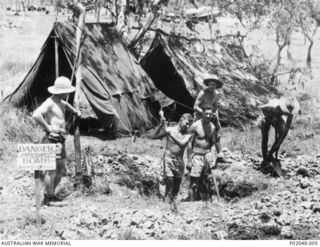 Port Moresby, New Guinea. 1943. Members of a RAAF Bomb Disposal Unit working at an unexploded bomb site. Two men are digging in the pit. A sign next to the pit reads "Danger Bomb." Identified is ..