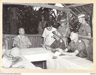 KAHILI, SOUTH BOUGAINVILLE. 1945-09-09. MAJOR F.A. GODING, BUIN LIAISON GROUP, 2 CORPS (3) THROUGH LIEUTENANT TATSU, THE JAPANESE INTERPRETER (2), READS INSTRUCTIONS TO MAJOR GENERAL MAGATA, ..